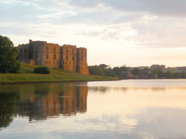 A ruined castle viewed at twilight across a calm pond