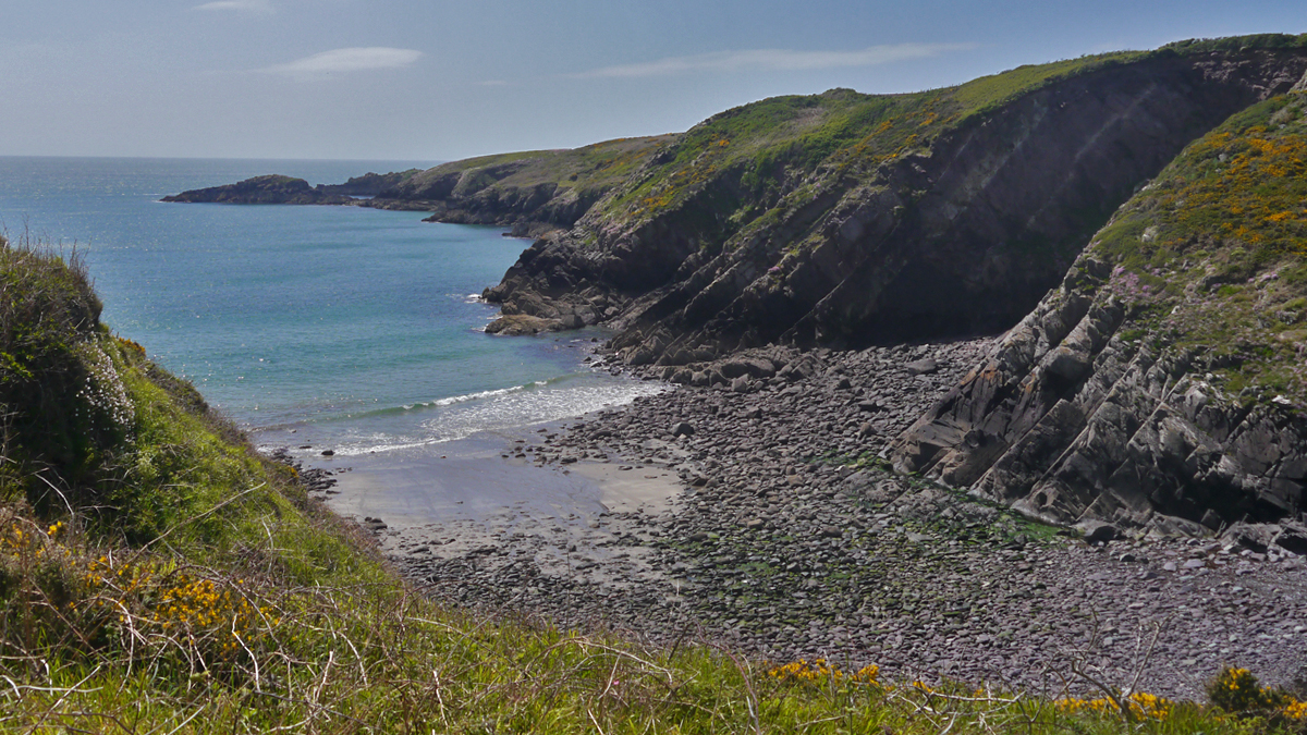 Rocky bay with a little sand surrounded by craggy cliffs topped with grass