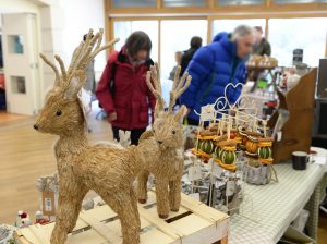 Reindeer decorations made from wood on a market stall with people browsing in the background