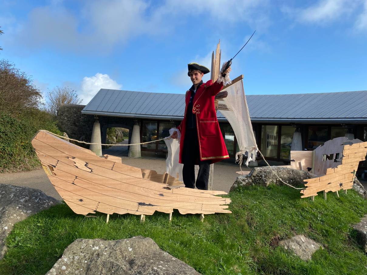 A pirate in a red coat and tricorn hat stands outside Oriel y Parc